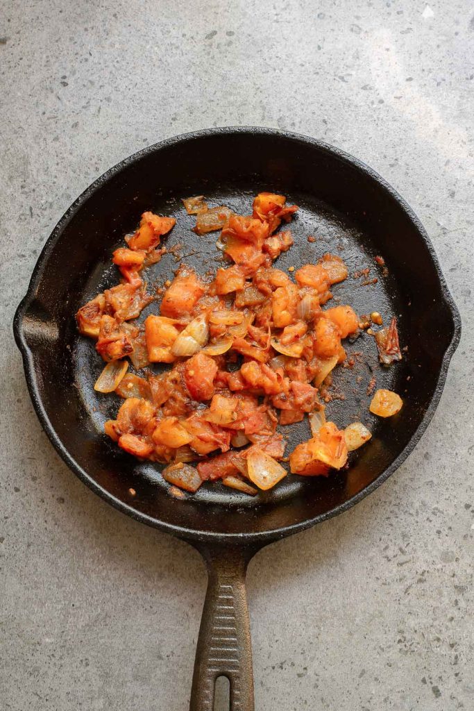 A cast iron skillet containing sautéed tomatoes and onions—classic ingredients for Menemen, a flavorful Turkish breakfast dish—sits on a gray countertop.