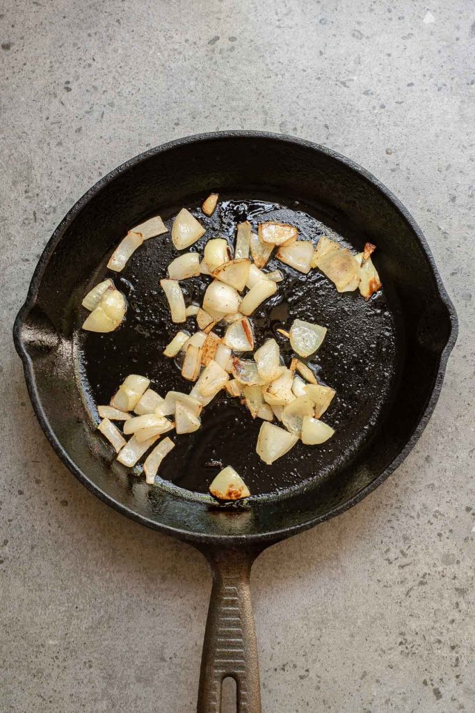 Chopped onions being sautéed in a black cast iron skillet on a gray countertop, the perfect start for making traditional Menemen, a flavorful Turkish breakfast dish.