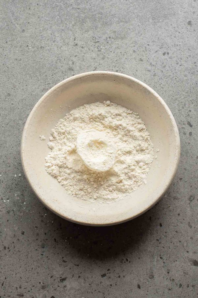 A white ceramic bowl filled with a mound of flour on a gray speckled countertop, perfect for preparing dishes like fried deviled eggs.