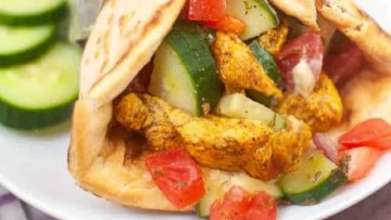 Chicken gyro with sliced cucumbers and diced tomatoes in pita bread, served with cucumber slices on the side.