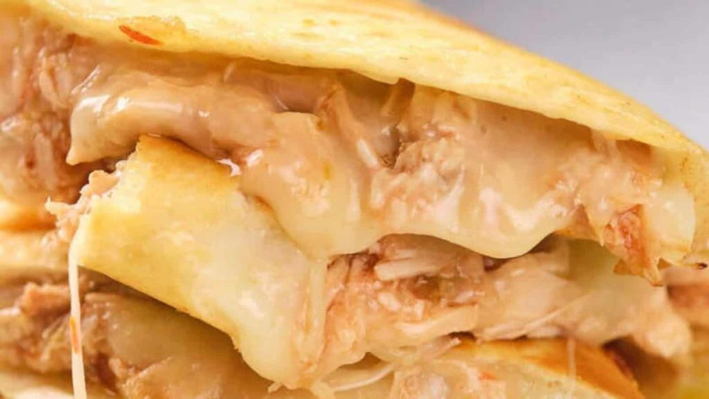 Close-up of a quesadilla filled with melted cheese and shredded meat, with the cheese visibly oozing out between the crispy tortilla layers.