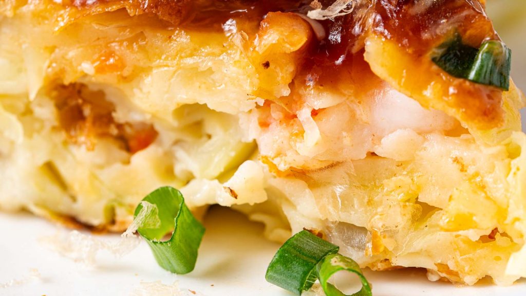 Close-up of a savory pastry slice filled with shrimp, vegetables, and topped with chopped green onions.