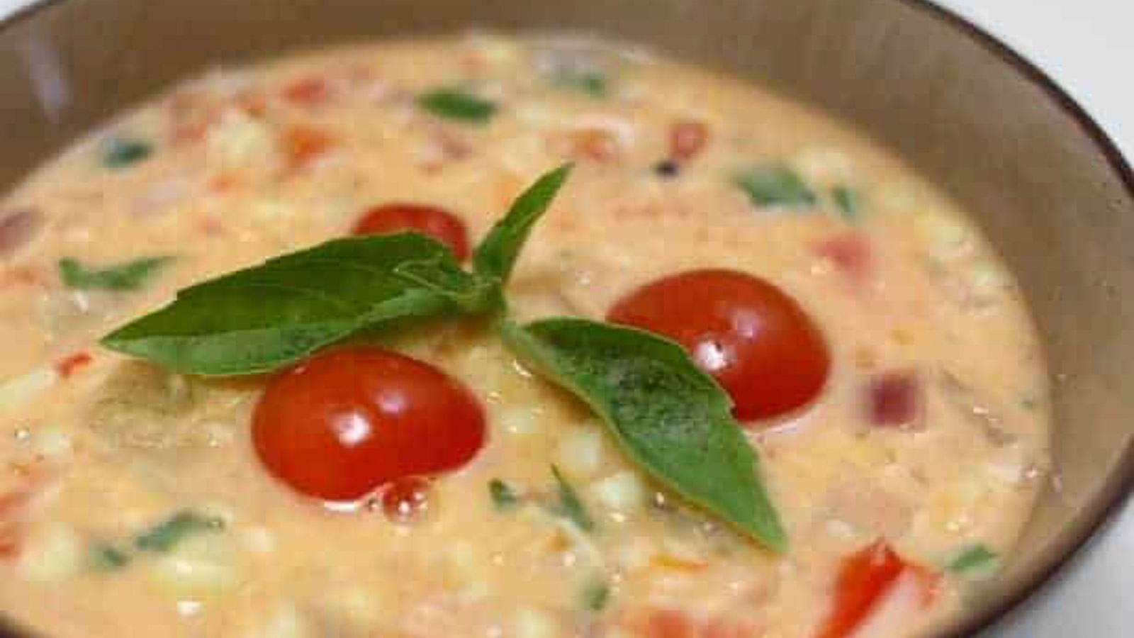 A bowl of corn and tomato soup with fresh basil.
