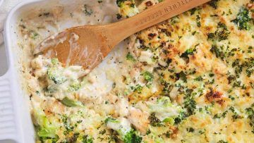 Baked chicken and broccoli casserole in a white dish, with a wooden spoon resting on top and a portion already served.