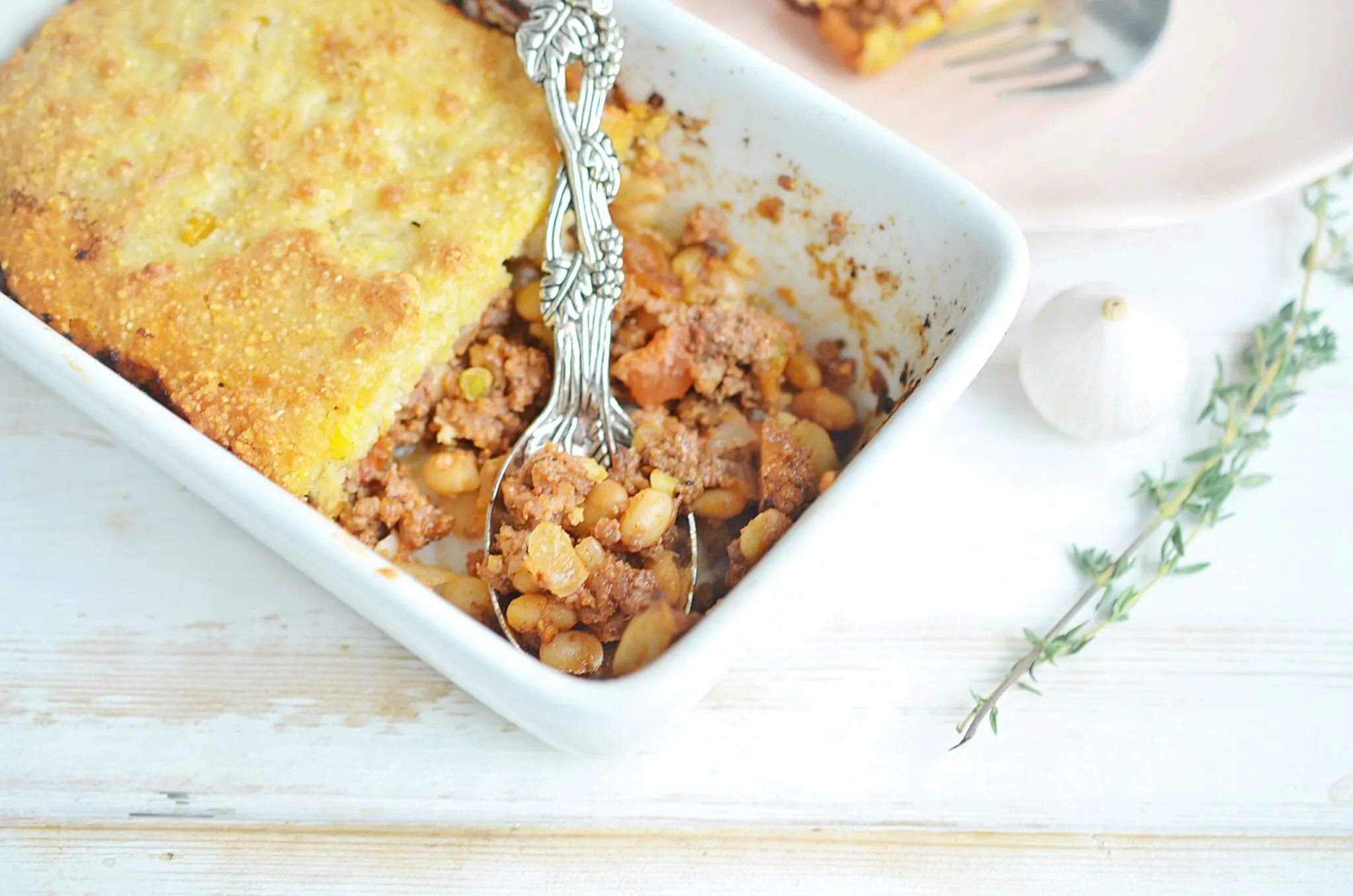 A white casserole dish with cornbread casserole and a silver serving spoon.
