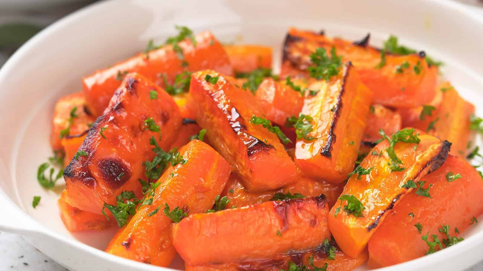 Roasted carrot pieces garnished with chopped parsley, served in a white dish.