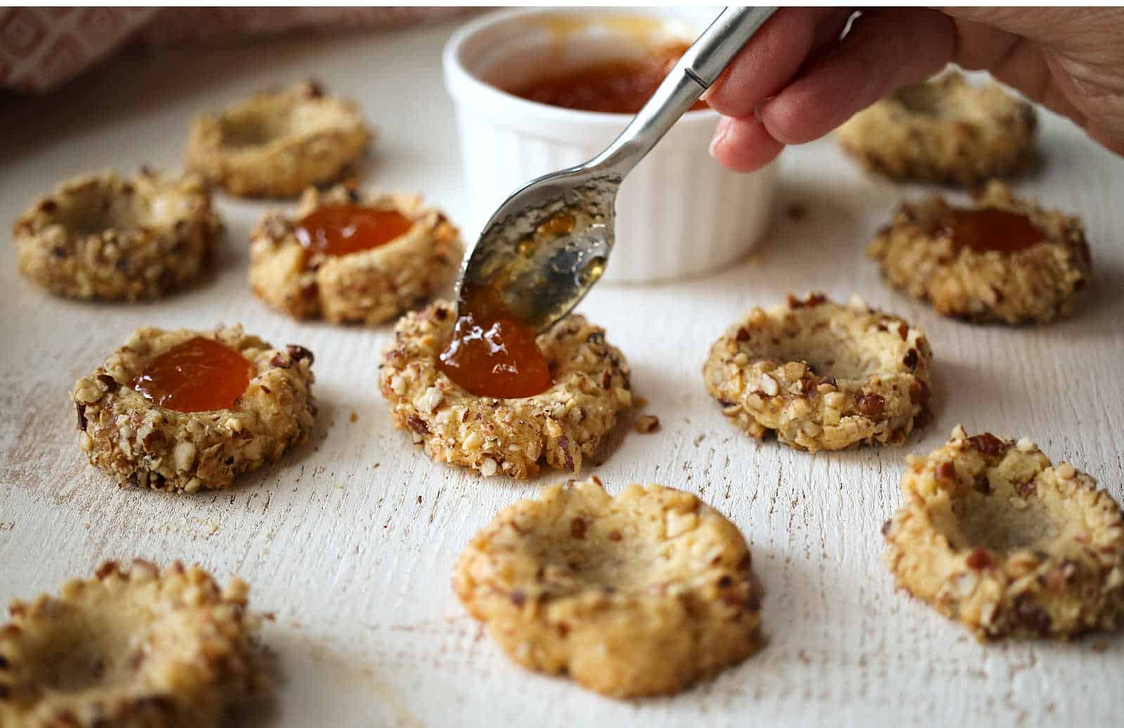 Spooning apricot jam into pecan thumbprint cookies.