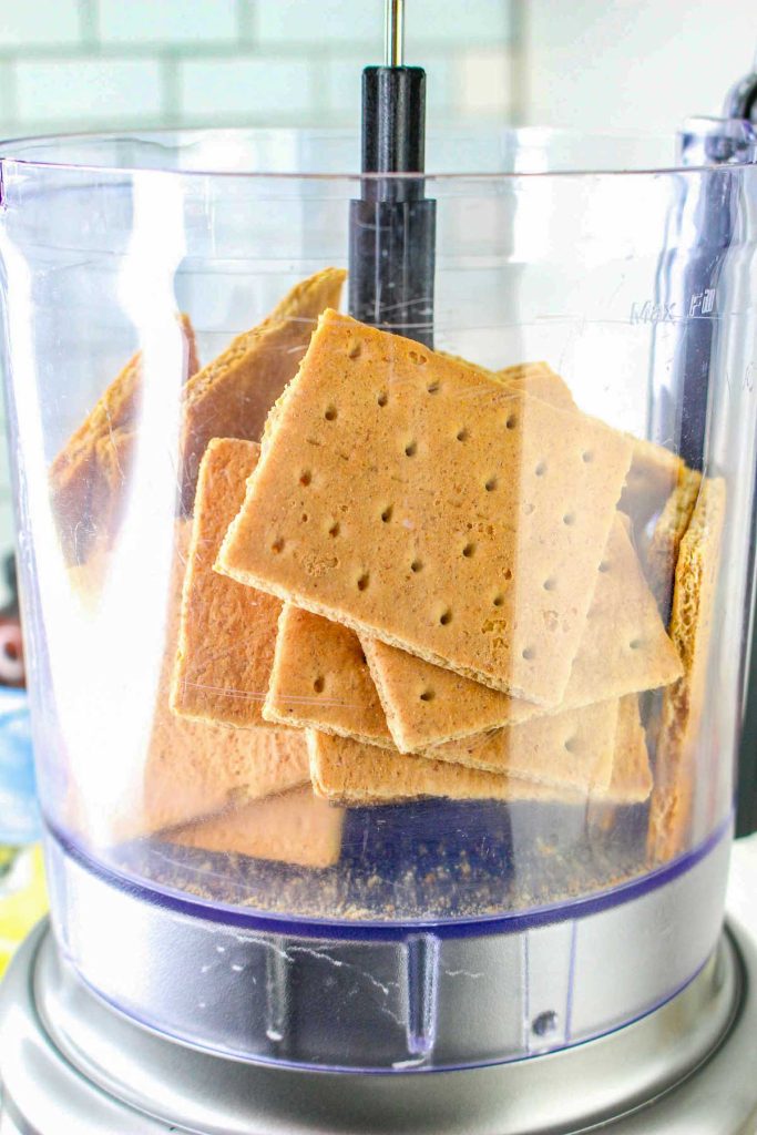 Stack of graham crackers inside a food processor bowl, ready to be crushed for delicious Banana Pudding Cheesecake squares.