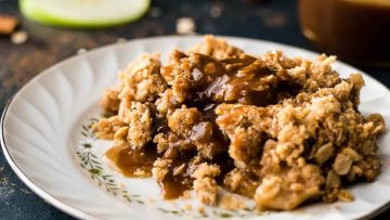 A serving of apple crisp topped with caramel sauce on a decorative white plate.