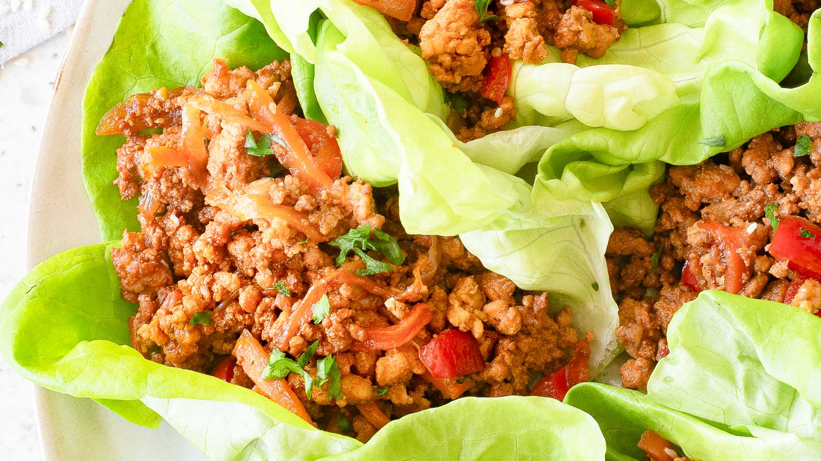 Three lettuce leaves filled with seasoned ground meat, diced red peppers, and chopped herbs, served on a plate.