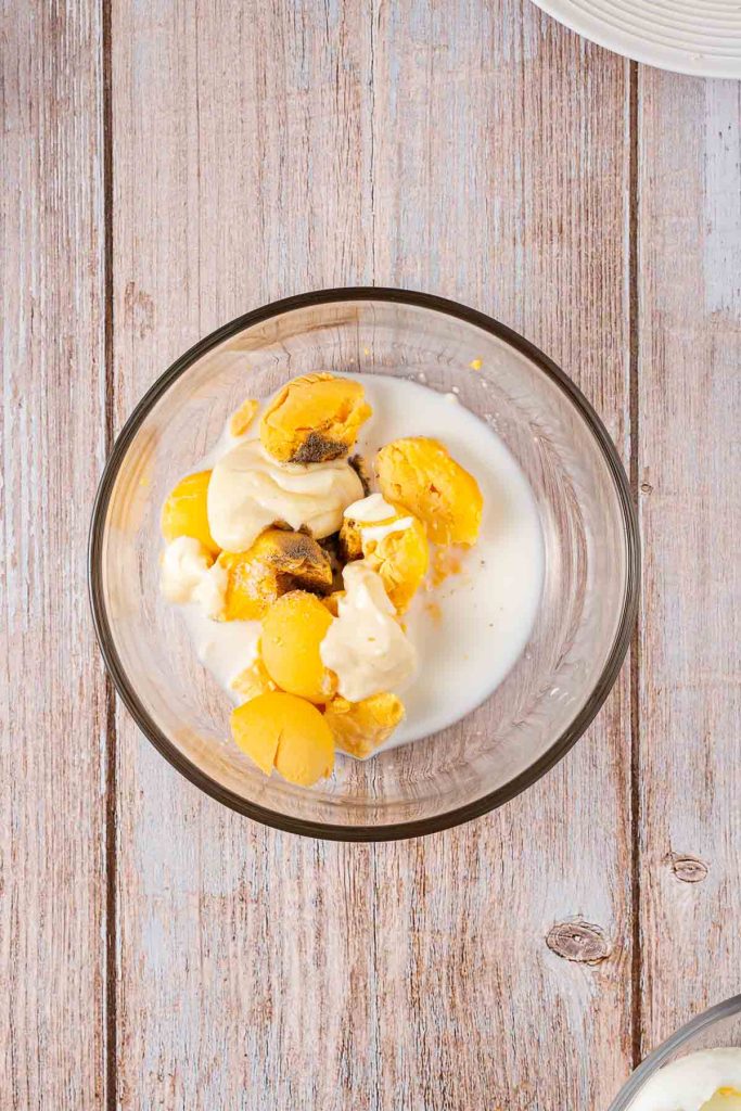 A glass bowl containing cooked yellow potatoes, mayonnaise, and milk on a wooden surface—perfect for making a creamy Japanese Egg Sandwich filling.